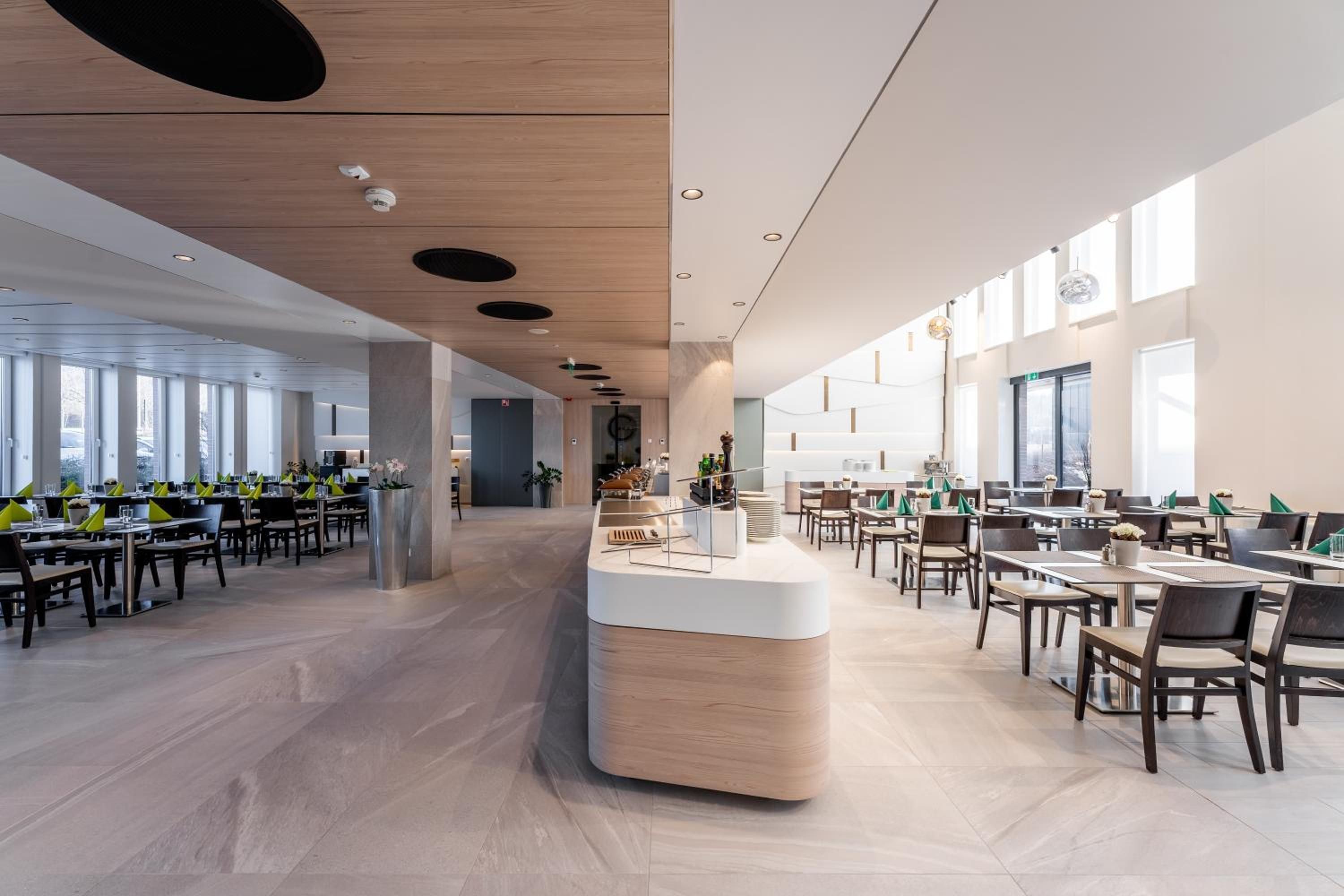 Un comedor amplio y moderno con múltiples mesas y sillas, una barra central y ventanas grandes que dejan entrar luz natural.