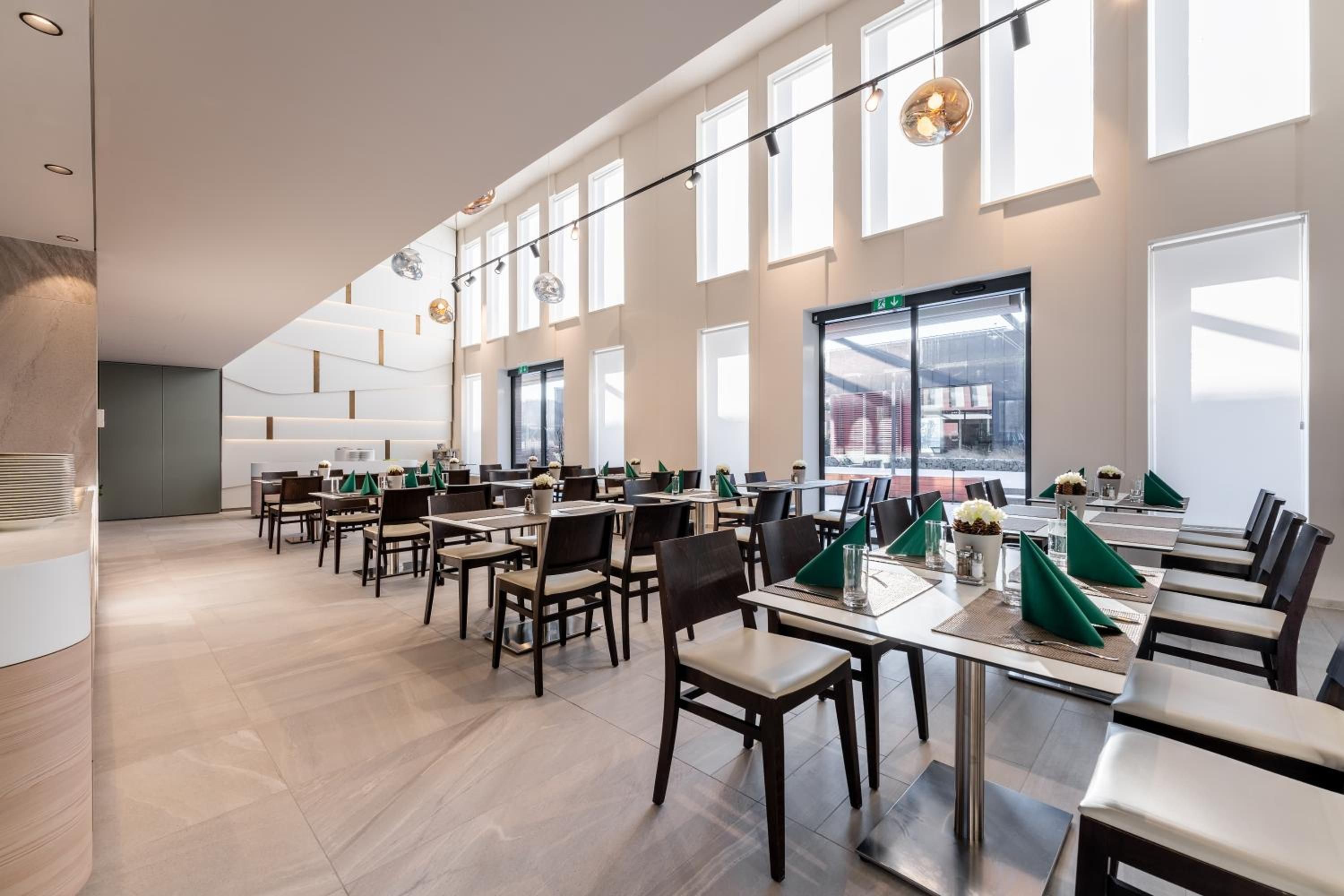 A spacious dining area with multiple tables and chairs, large windows, and a modern interior design.