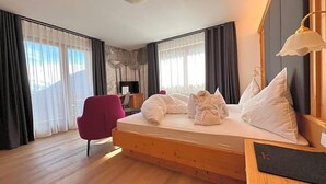 Una habitación de hotel con cama de madera, escritorio, silla y un ventanal con cortinas.
