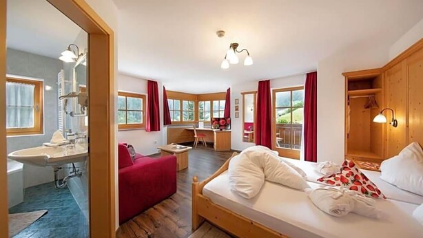 Un dormitorio con cama de madera, un escritorio, una silla roja y vistas al exterior a través de amplias ventanas.