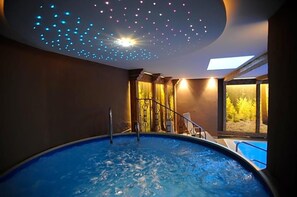 A hot tub with a ceiling that has a starry light projection, a view of a forest through a large window, and a pool adjacent to the hot tub. - Bergfrieden (Martello)