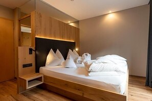 A modern hotel room with a wooden bed frame, a built-in headboard, and a small wooden bench. - Bergfrieden (Martello)