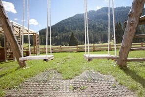 Un columpio de madera en un área con césped, con montañas al fondo.