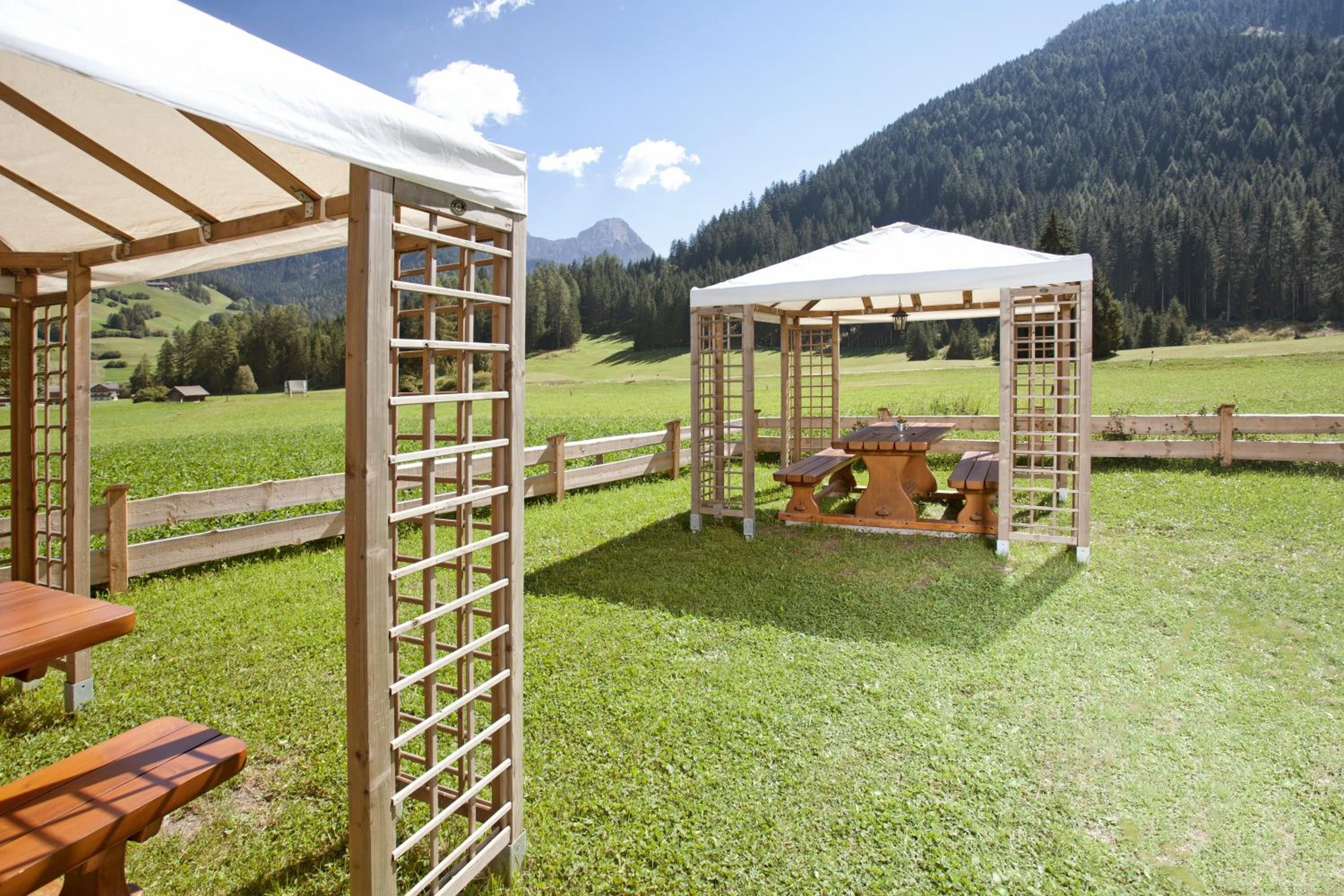 A wooden pergola with a table and benches, a covered seating area, and a view of a mountainous landscape.