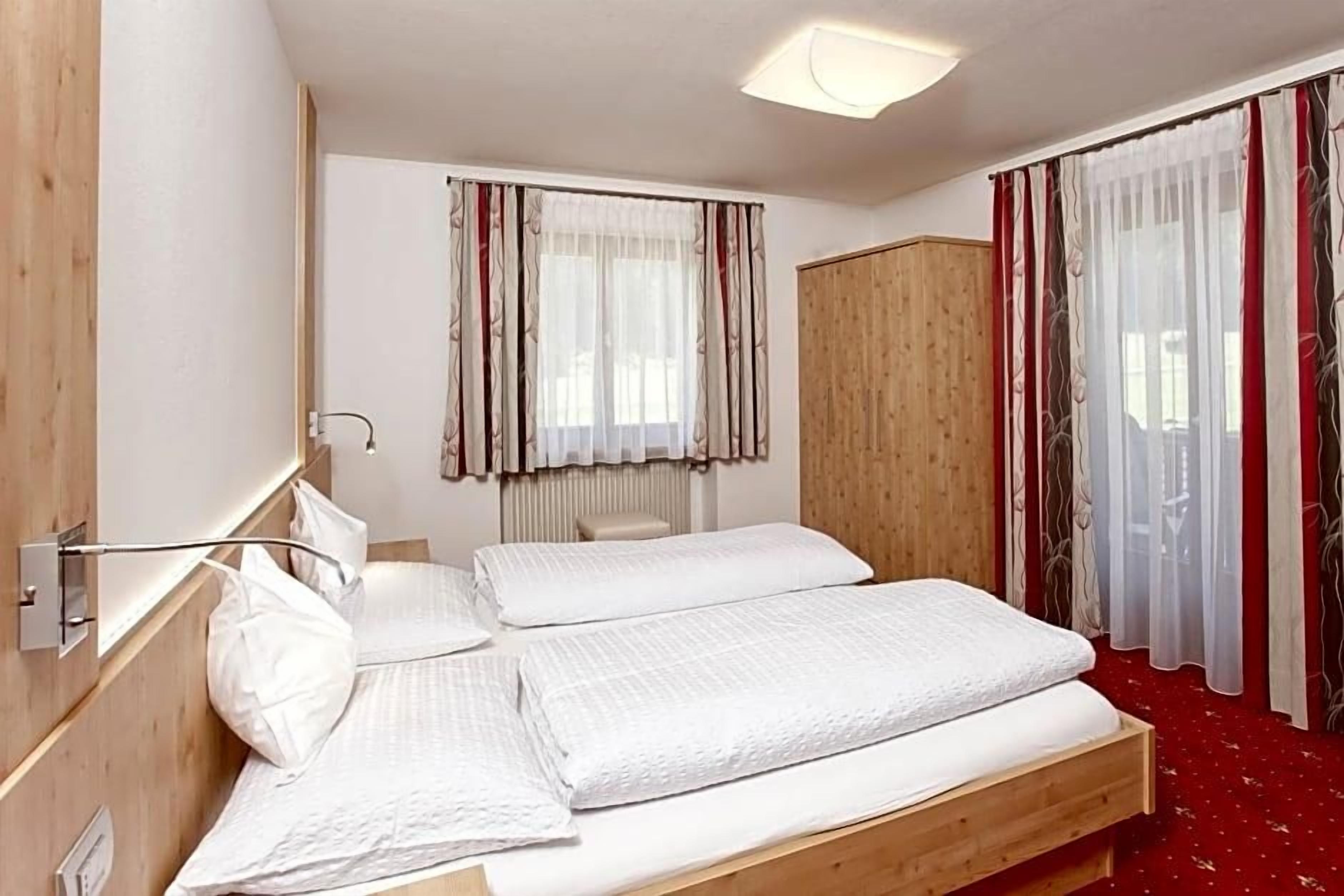 Une chambre d’hôtel avec un lit en bois, une armoire et une fenêtre avec des rideaux.