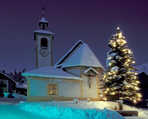 Una iglesia cubierta de nieve con una torre de reloj y un árbol de Navidad decorado.