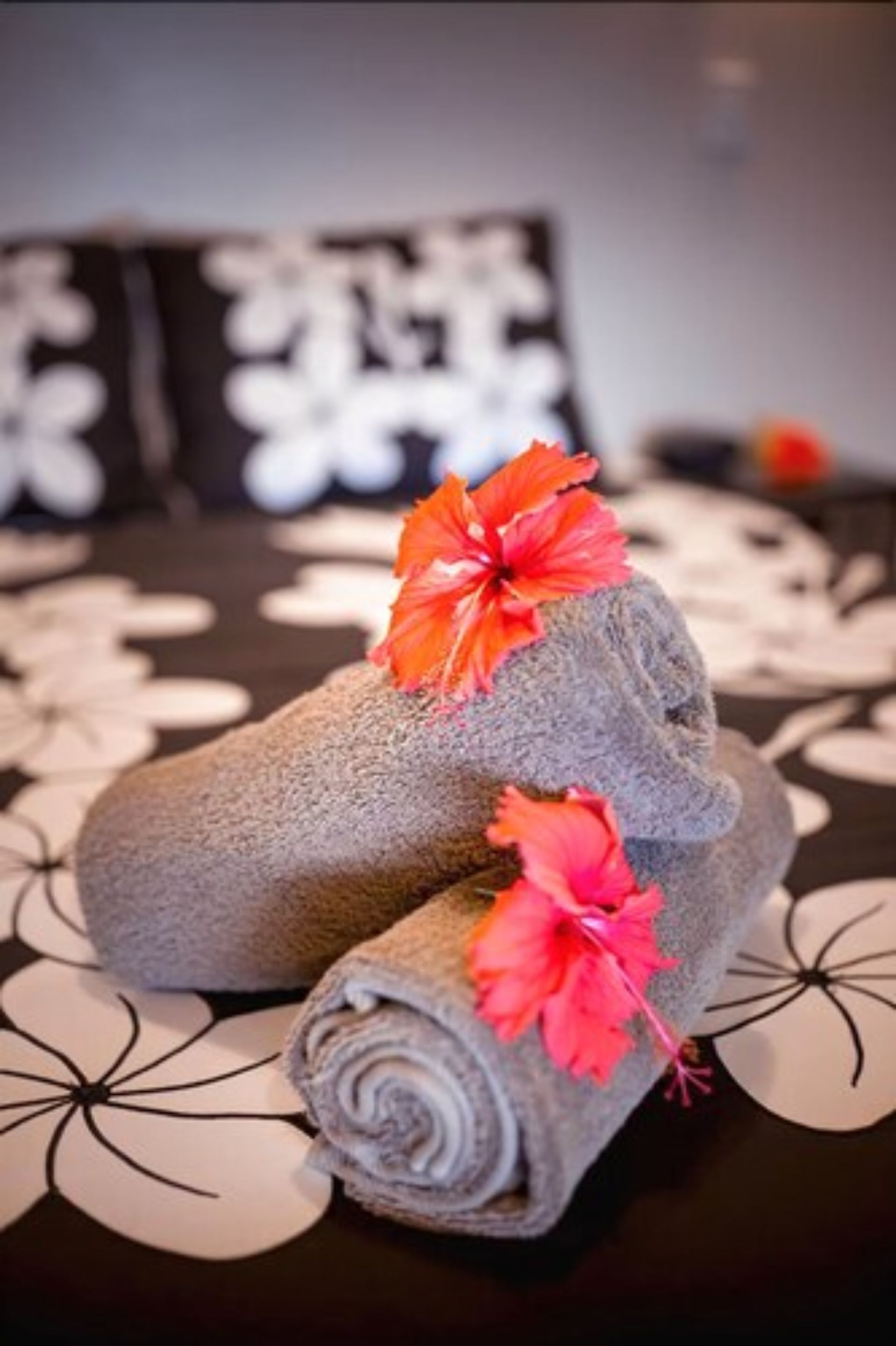 A neatly folded towel with a hibiscus flower on a bed with a black and white floral bedspread.