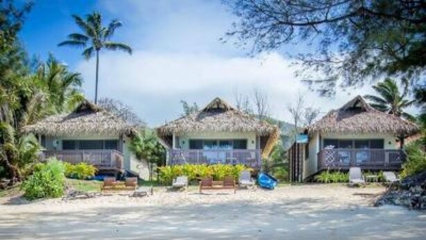 Una propiedad frente a la playa con cabañas de techo de paja, agua turquesa cristalina y exuberante vegetación.