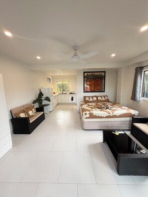 A modern bedroom with a large bed, a sofa, a small kitchen area, and a dining table. - Muri Shores (Rarotonga)
