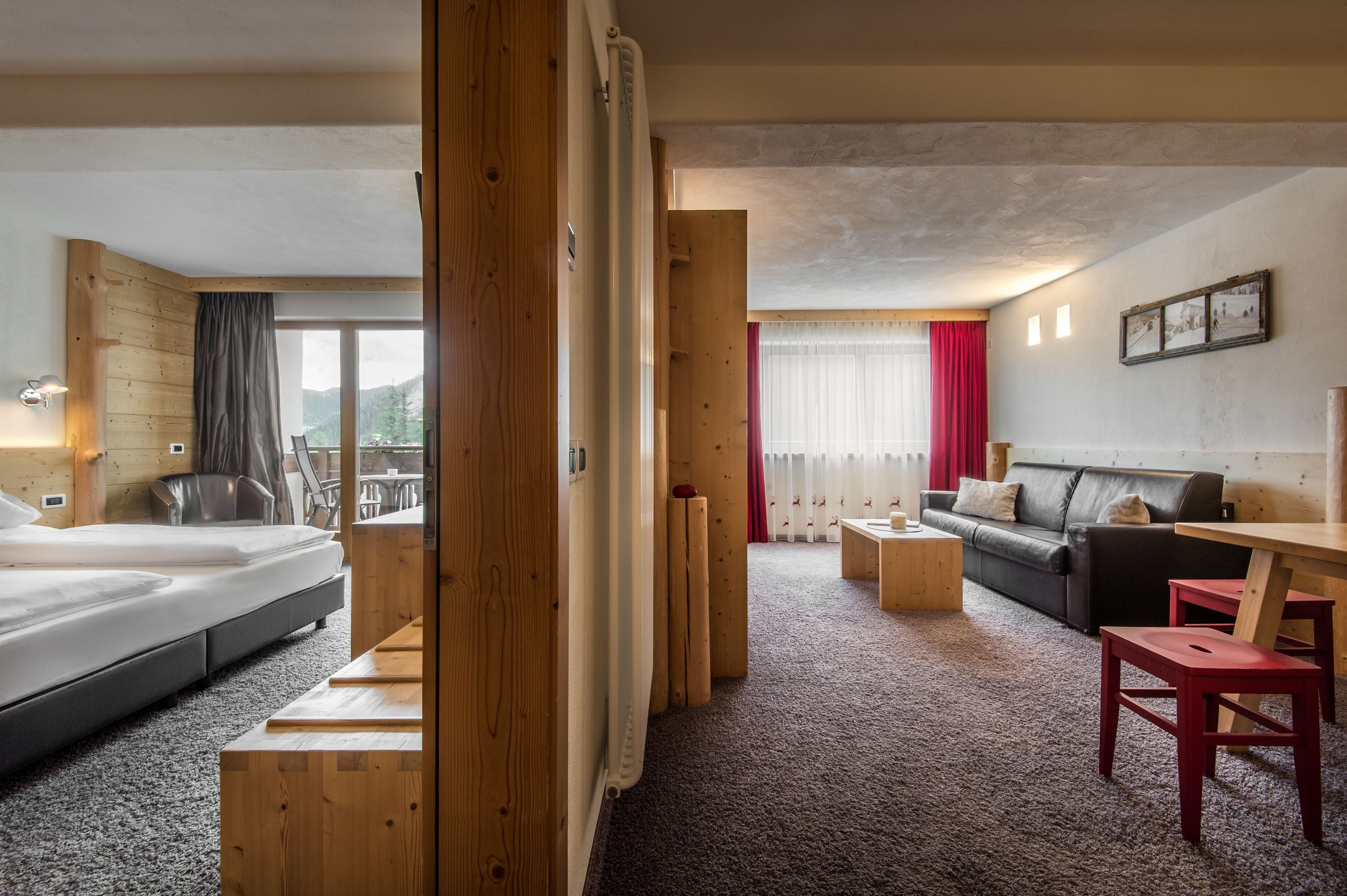 A hotel room with a bed, a wooden desk, a sofa, and a view of the outdoors.