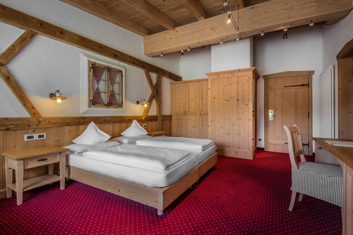 A bedroom with a wooden ceiling, a bed with white bedding, a red carpet, and a wooden wardrobe.