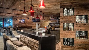 A bar area with a wooden ceiling, multiple pendant lights, and shelves displaying bottles. - Hotel Gran Ciasa (Corvara in Badia)