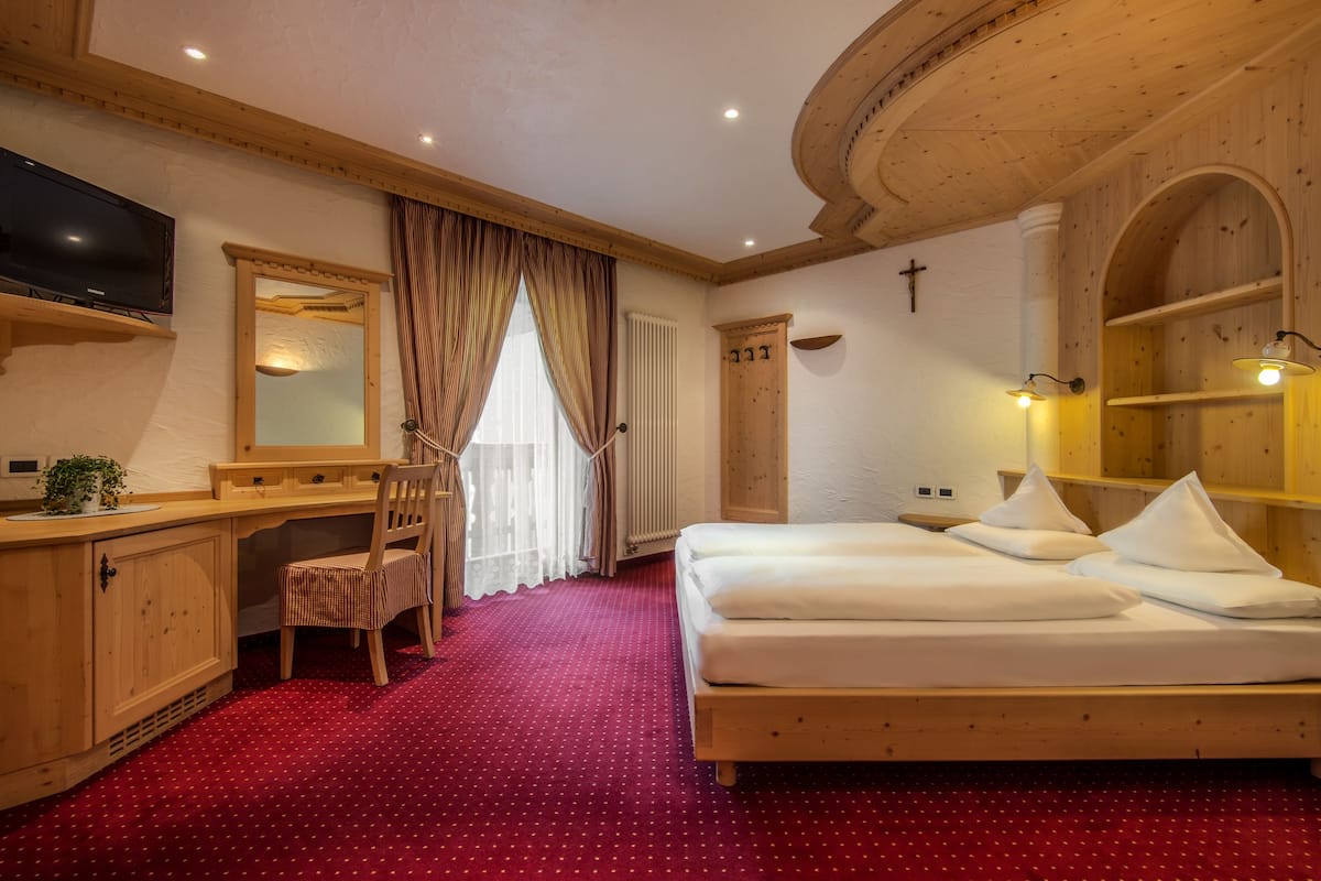 A hotel room with a wooden bed, a desk with a chair, a TV, and a large mirror.