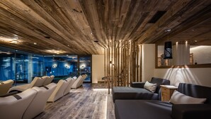 A modern interior with a wooden ceiling, leather sofas, and a glass wall with city views. - Hotel Gran Ciasa (Corvara in Badia)