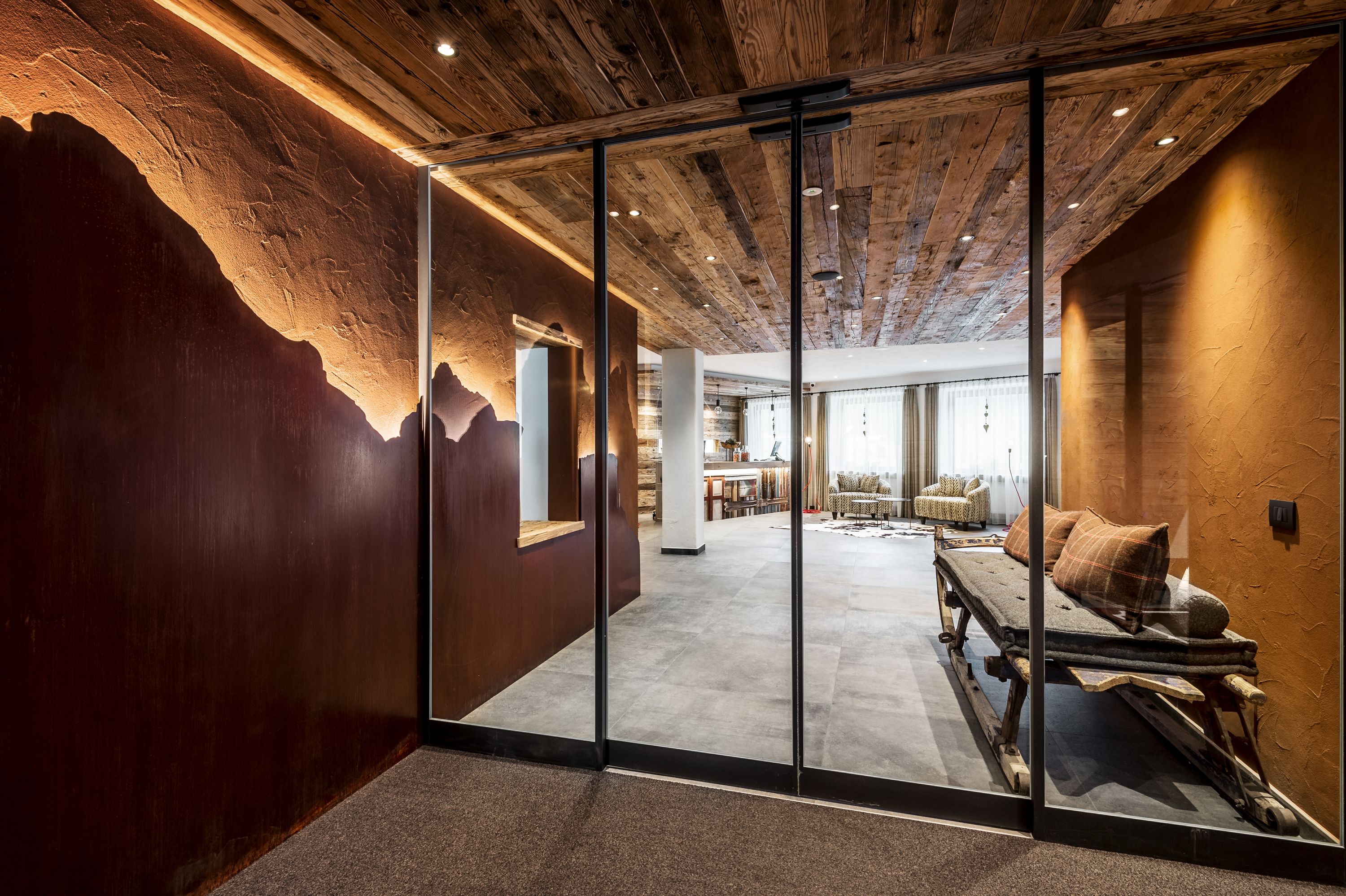 Een modern interieur met een houten plafond, glazen wanden en een gezellige zithoek met een bank en kussens.