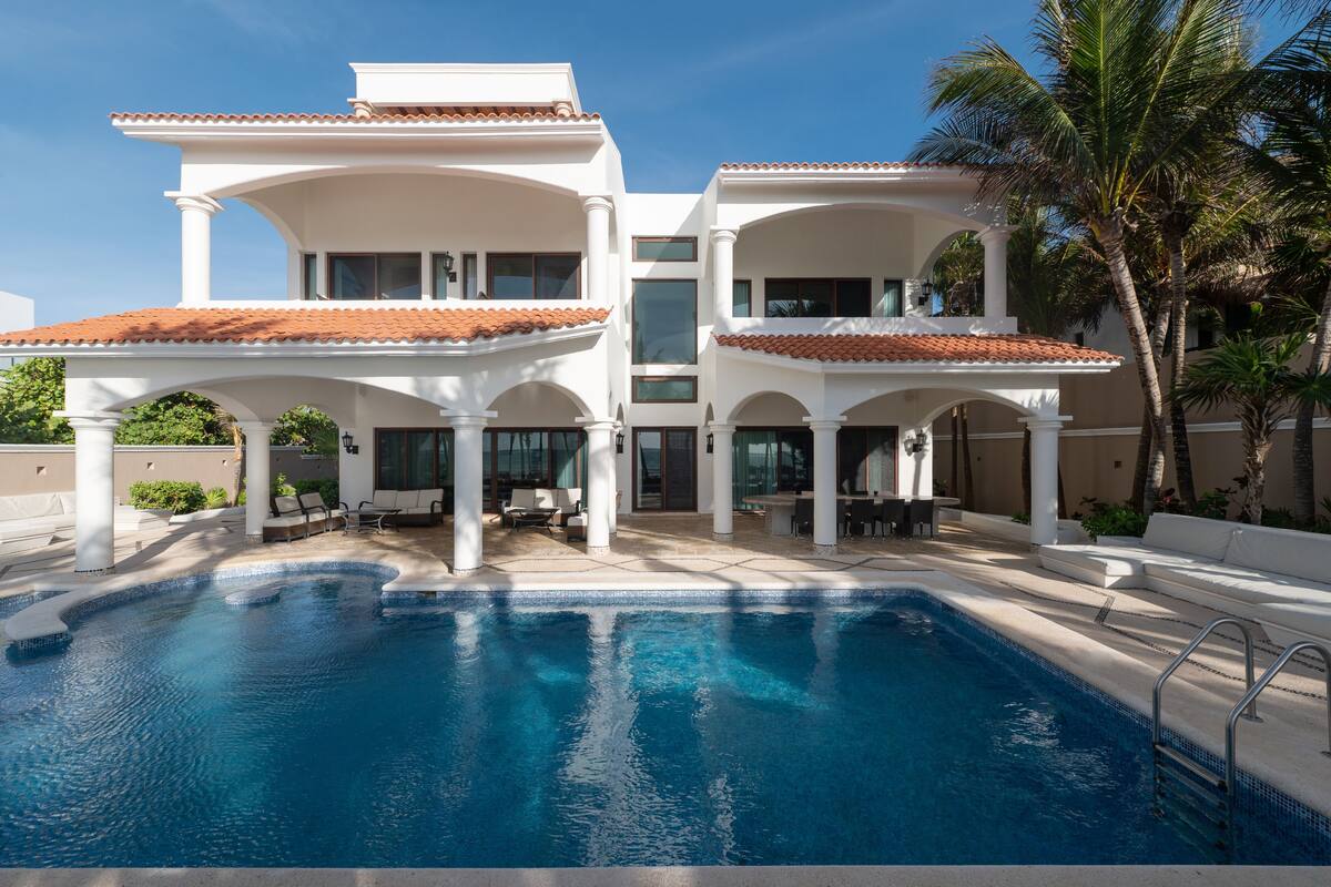A modern resort with a large pool, covered outdoor seating, and a two-story building with a tiled roof.