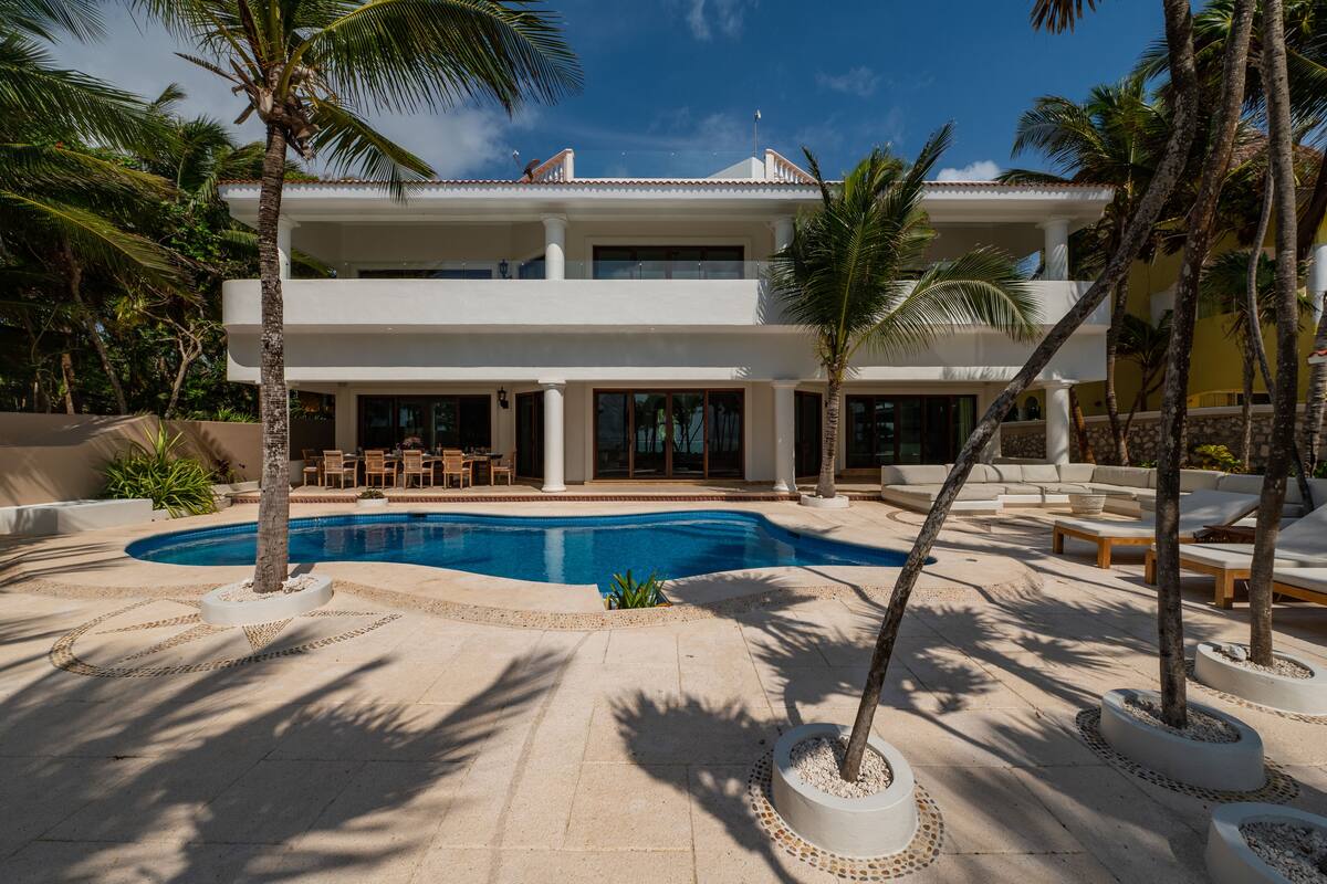 A two-story building with a swimming pool, outdoor seating, and palm trees.