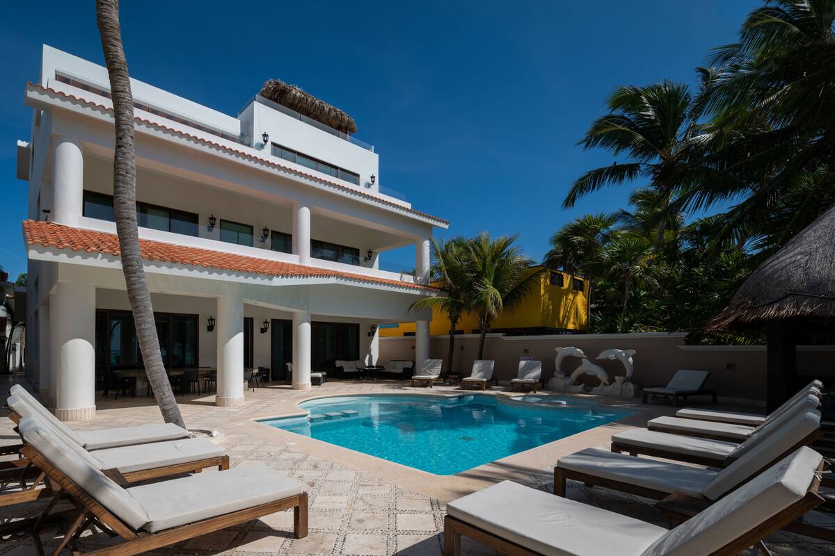 A poolside area with lounge chairs, a swimming pool, and a two-story building with balconies.