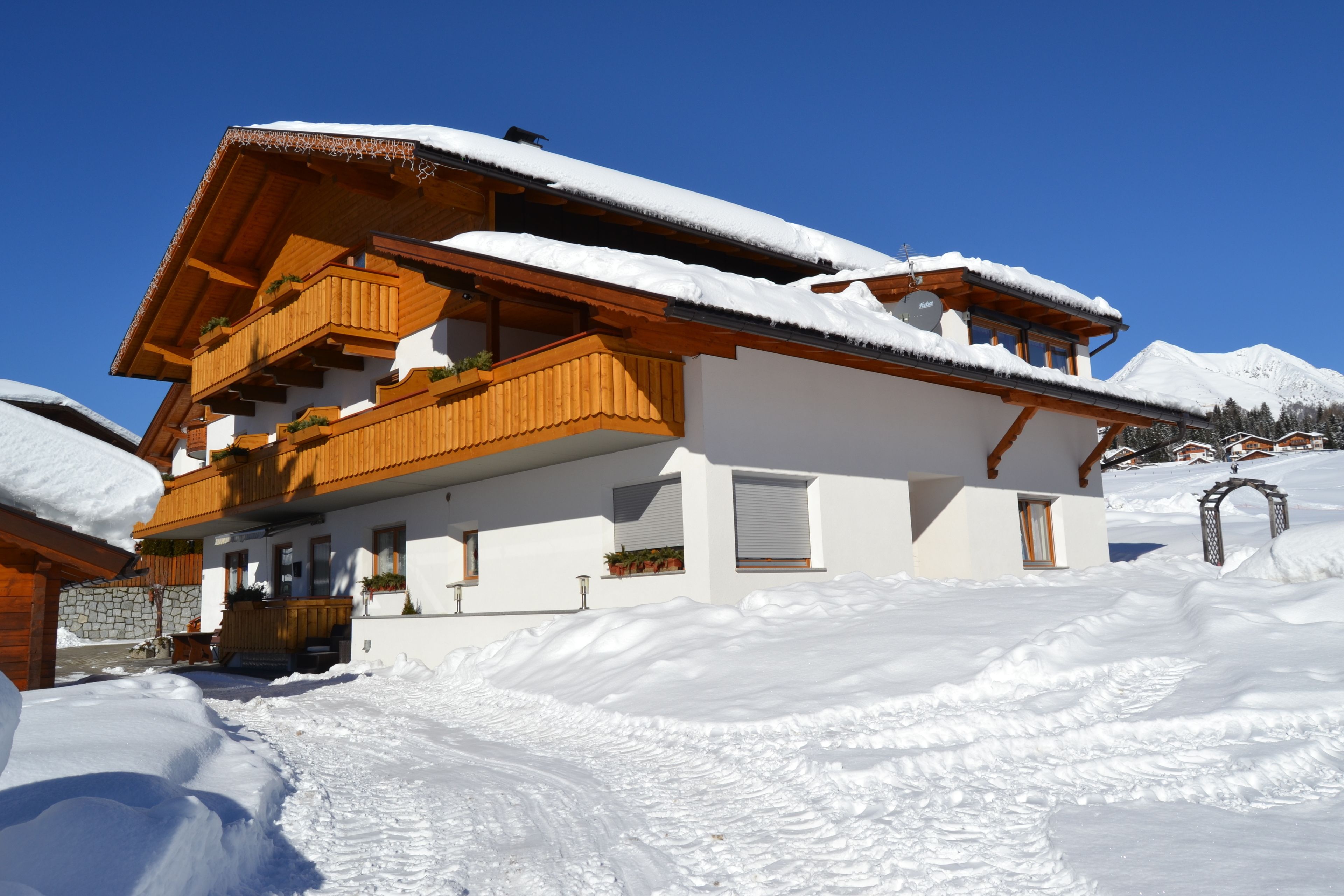 A multi-story chalet with wooden balconies, snow-covered roofs, and a stone wall foundation.