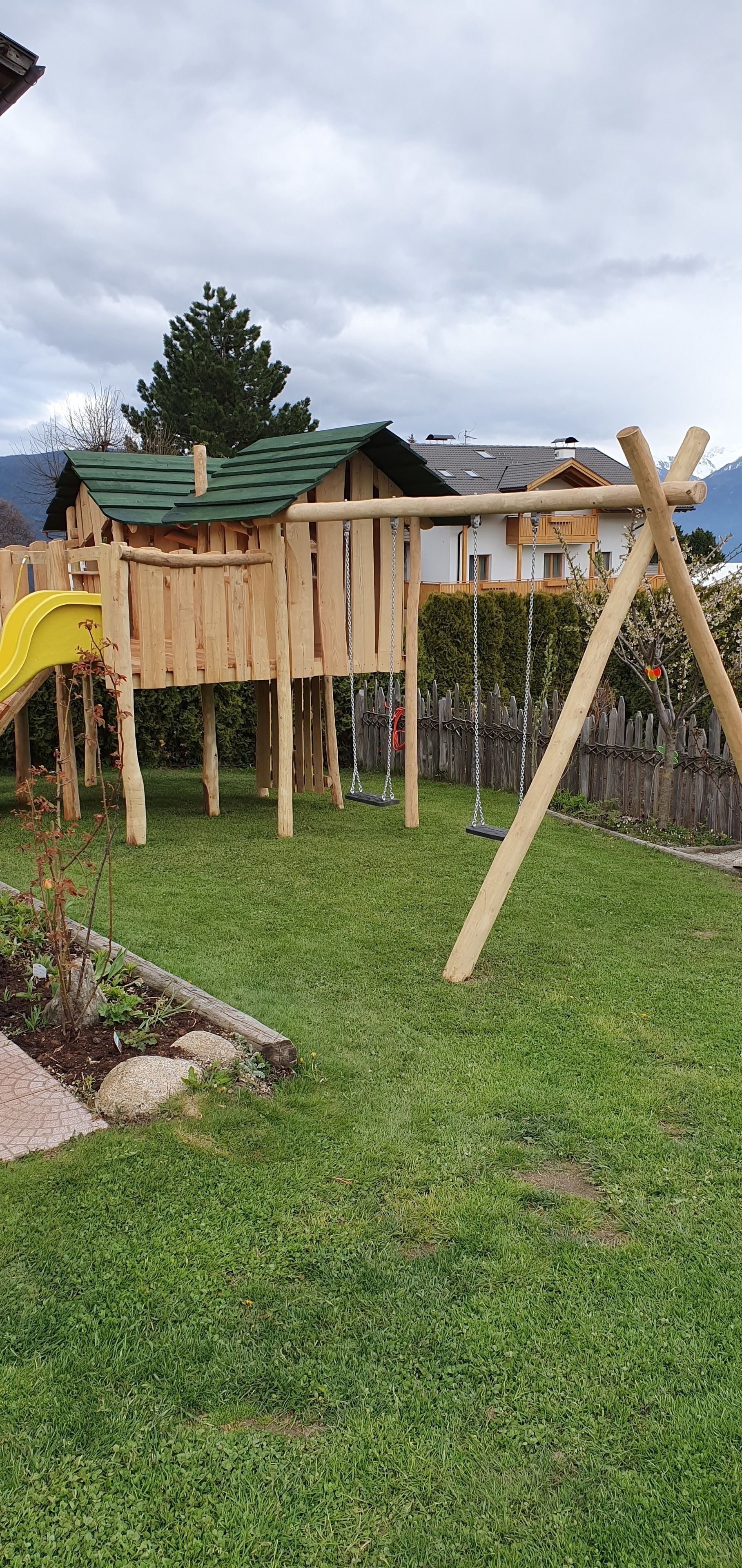 Een houten speeltoestel met een glijbaan en schommels in een achtertuin.
