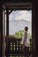 Una persona de pie en un balcón de madera con vistas a montañas y vegetación.