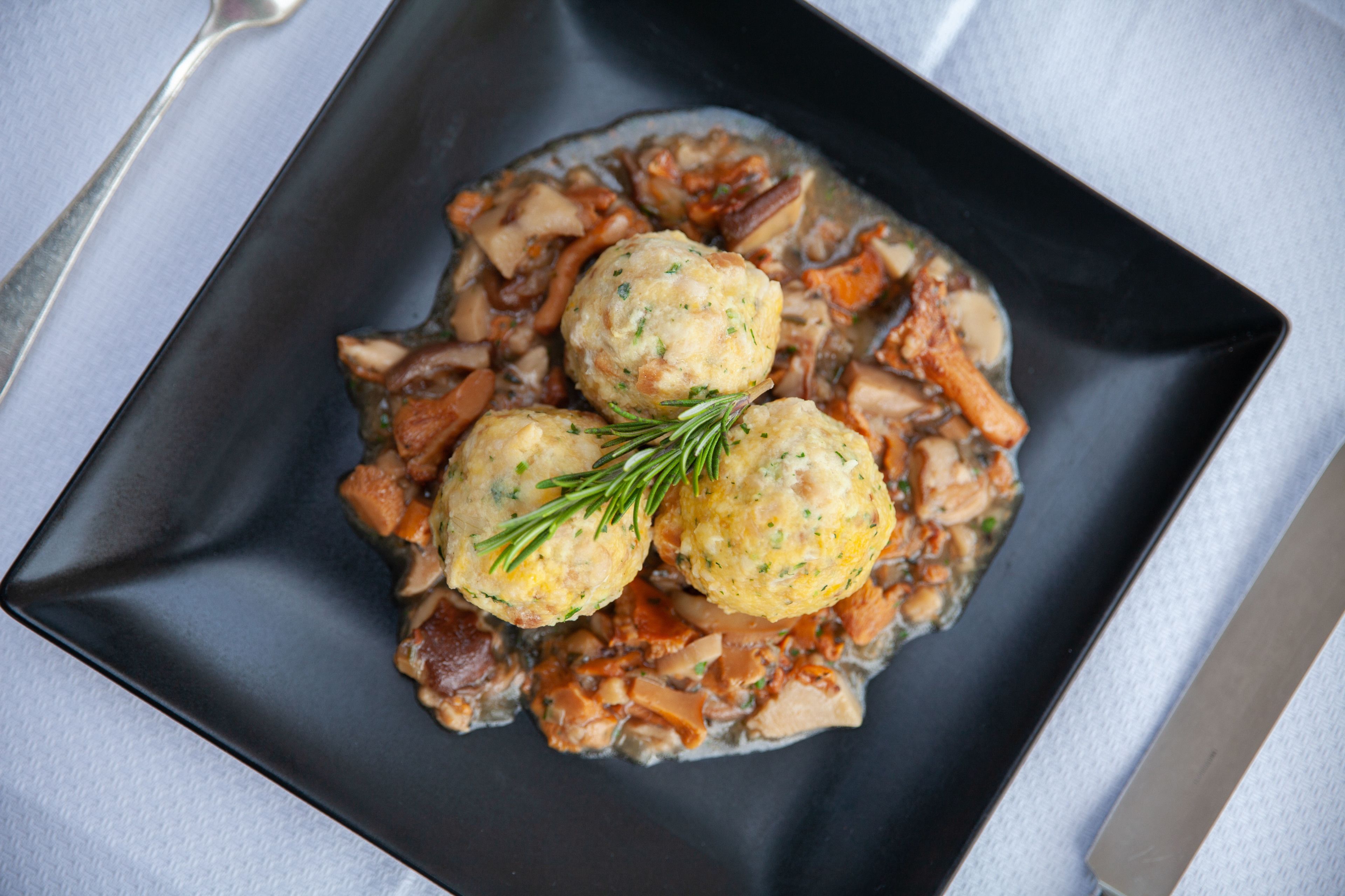 Un plato cuadrado con tres dumplings y una ramita de romero sobre una superficie oscura.