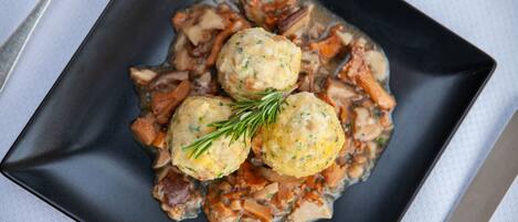Un plato cuadrado con tres dumplings y una ramita de romero sobre una superficie oscura.