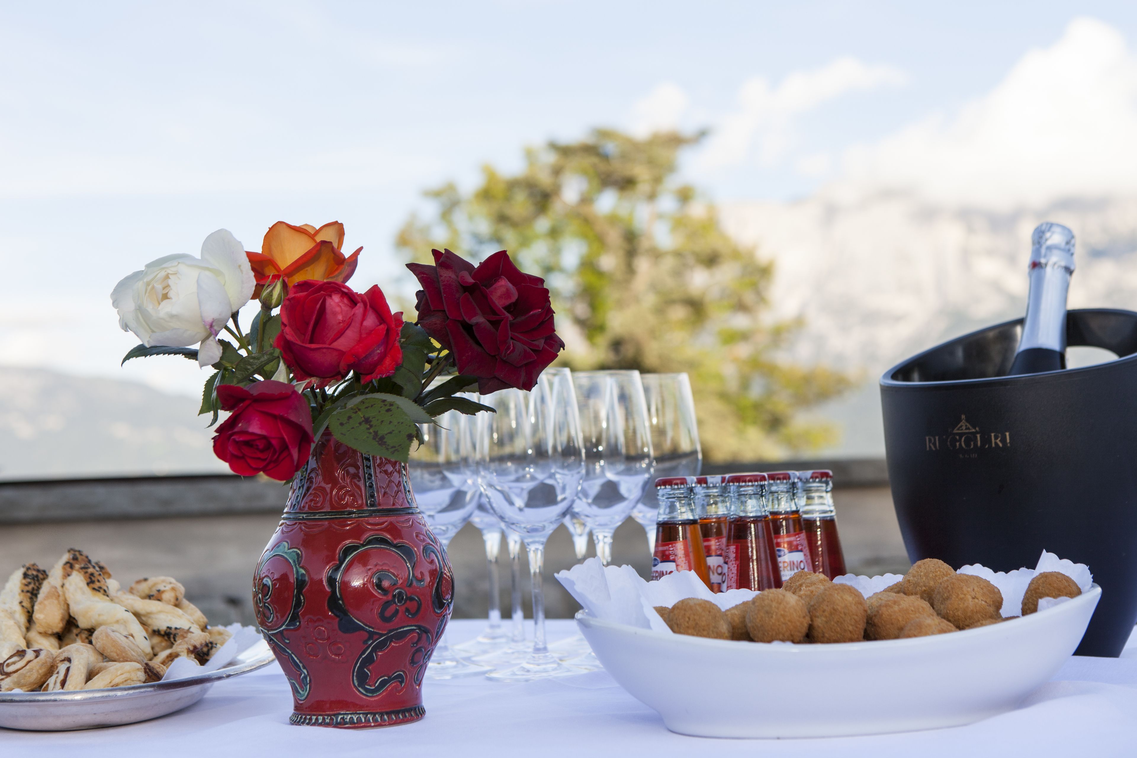 Una mesa con un florero decorativo de rosas, un bol de aperitivos, una botella de champán y una botella de salsa.