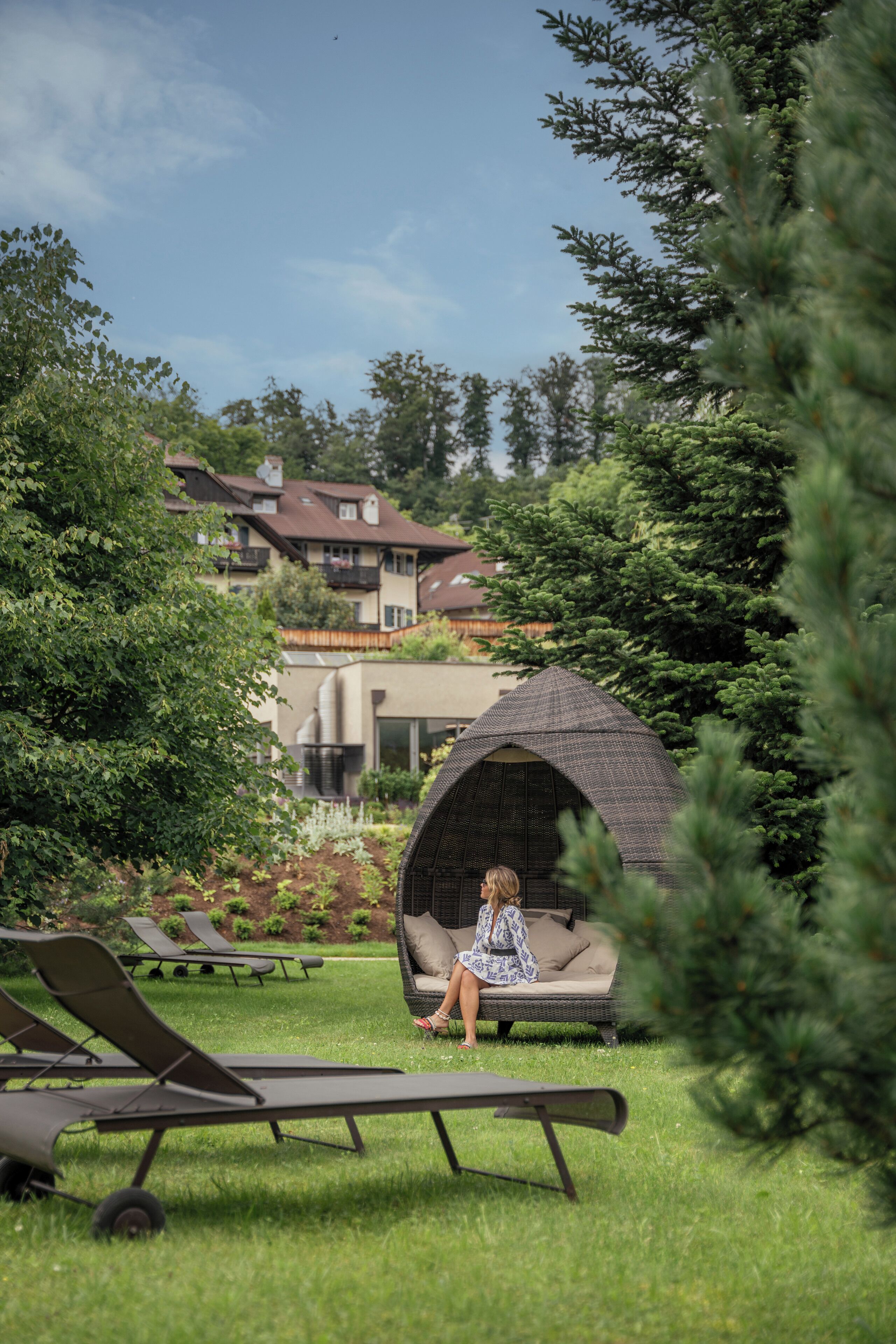 Um jardim com um gazebo, cadeiras de estar e uma pessoa sentada em um banco.