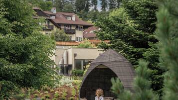 Um jardim com um gazebo, cadeiras de estar e uma pessoa sentada em um banco.