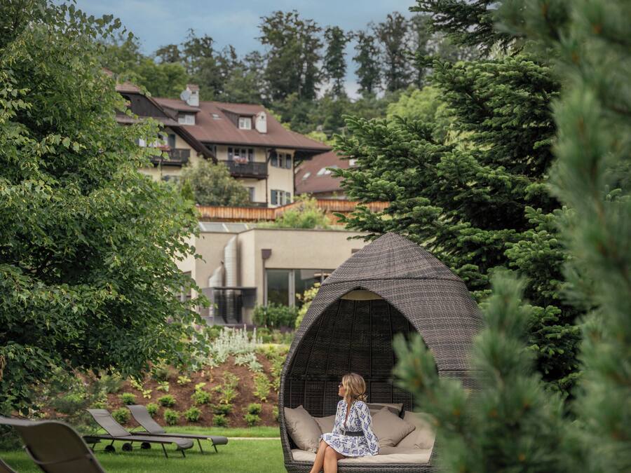 Um jardim com um gazebo, cadeiras de estar e uma pessoa sentada em um banco.