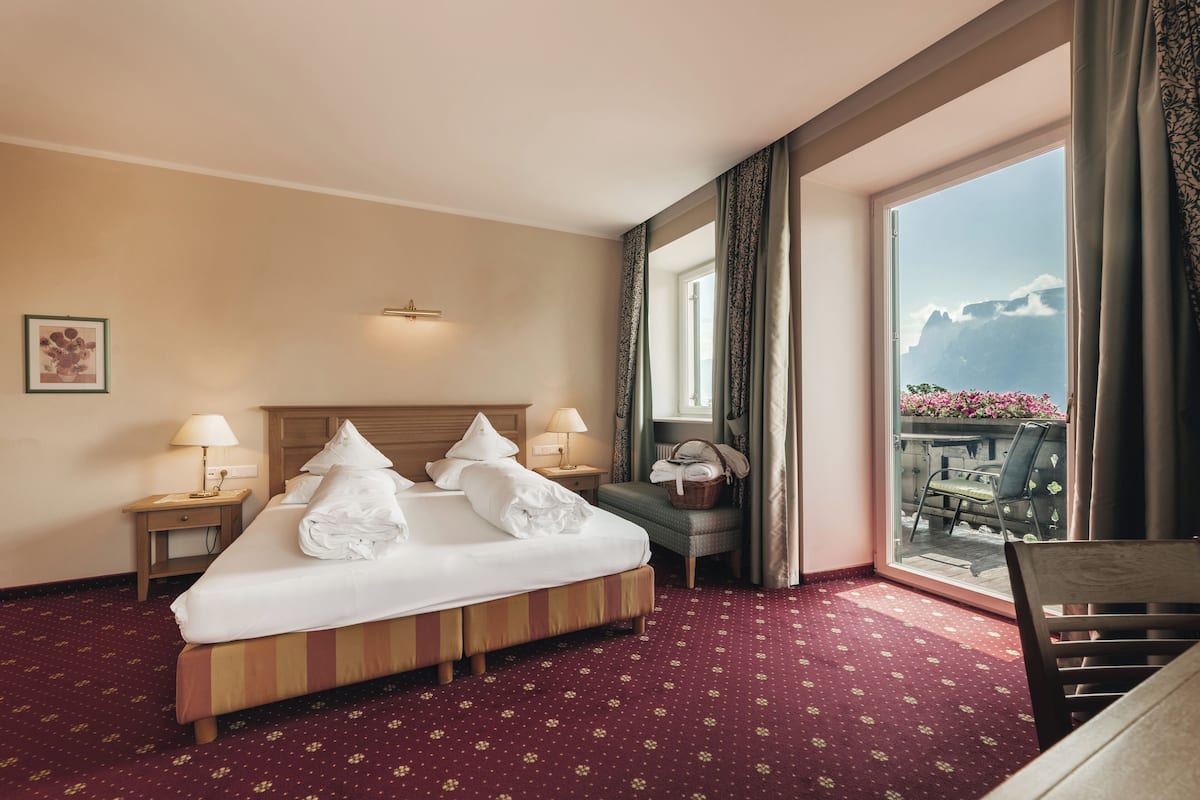 A hotel room with a bed, two bedside tables, a chair, a window with a view of mountains, and a red carpet.