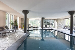 An indoor swimming pool with lounge chairs and a stone wall. - Bemelmans Post Hotel (Renon)