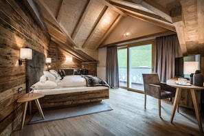 Habitación tipo cabaña de madera con cama en el altillo, un escritorio y vistas al exterior.