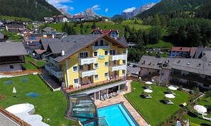 Un hotel de varios pisos con piscina y zona de estar al aire libre, rodeado por un paisaje montañoso.