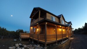 Une cabane en rondins à deux étages, dotée d’un porche et d’une terrasse couverte, et entourée d’un paysage naturel.