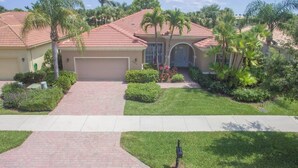 A residential house with a red-tiled roof, a garage, and a well-maintained lawn with palm trees. - Players Club Membership Available With Heated Pool (Naples)