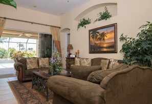 A living room with a sofa set, a coffee table, and a painting of a sunset. - Players Club Membership Available With Heated Pool (Naples)
