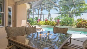 A glass-enclosed patio with a pool, outdoor furniture, and tropical plants. - Players Club Membership Available With Heated Pool (Naples)