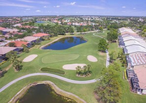 An aerial view of a golf course with a pond, sand bunkers, and a road curving through the property. - Players Club Membership Available With Heated Pool (Naples)