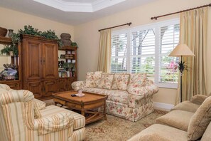 A living room with a floral sofa, striped armchairs, a wooden coffee table, and a large window with curtains. - Players Club Membership Available With Heated Pool (Naples)