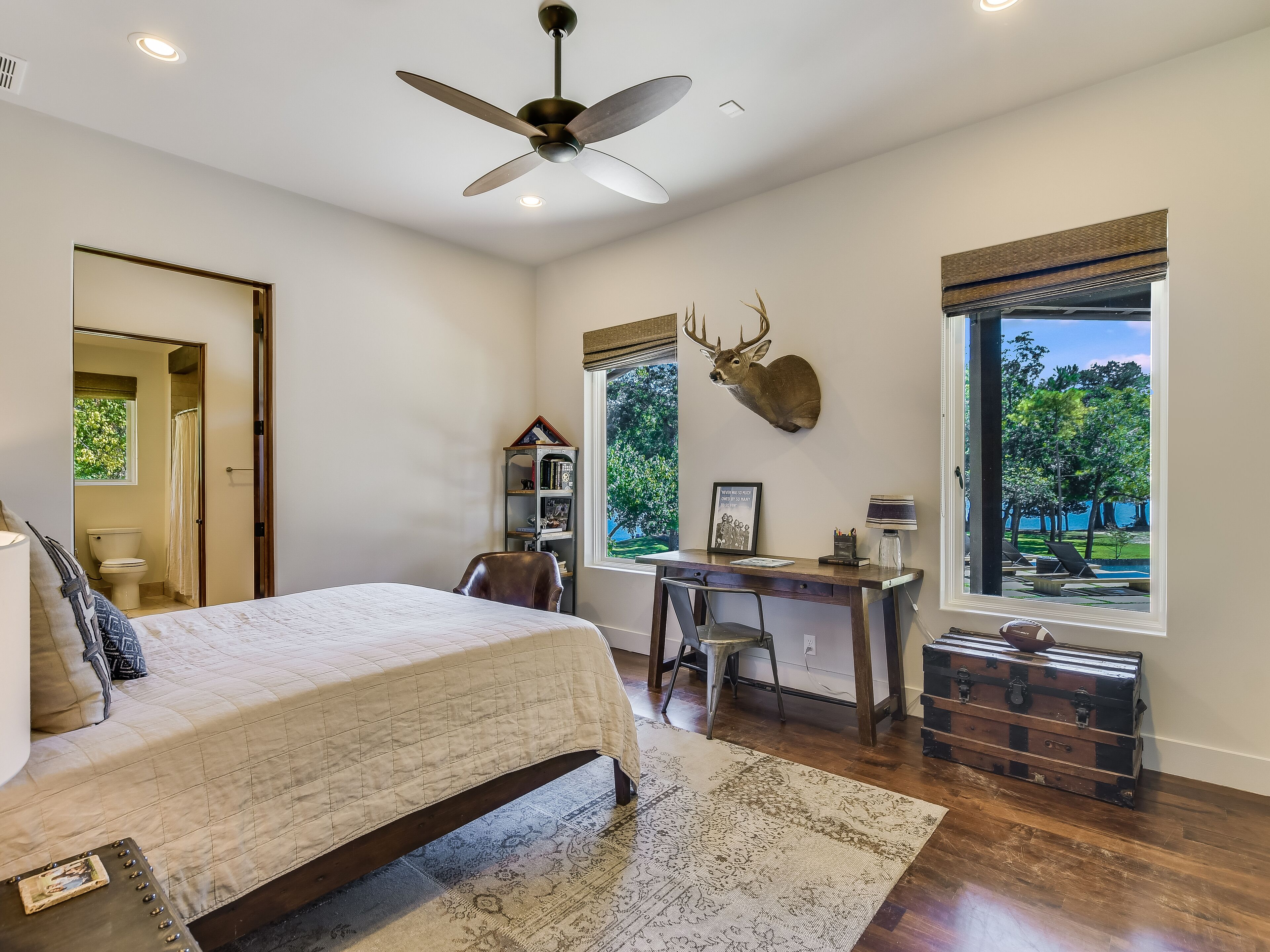 A bedroom with a bed, desk, chair, and a mounted deer head.
