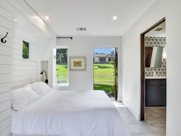 A bedroom with a large bed, a window, and a view of a garden.