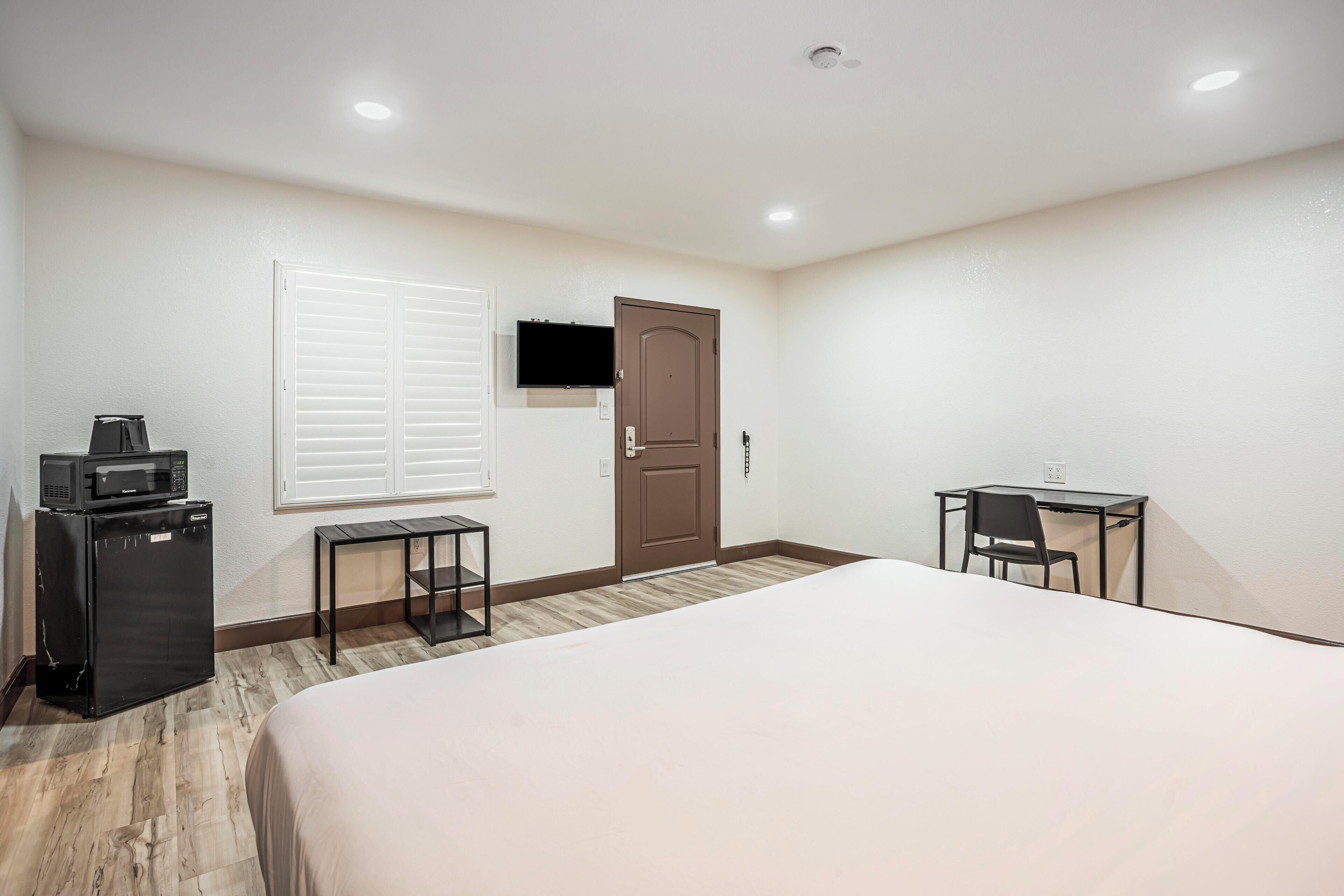 Ein Hotelzimmer mit einem großen Bett, einem Schreibtisch mit Stuhl, einem an der Wand befestigten Fernseher und einem Kühlschrank.