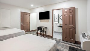 Ein Hotelzimmer mit zwei Betten, einem Schreibtisch, einem Fernseher und einem durch eine offene Tür einsehbaren Badezimmer.