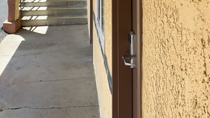 Ein Gebäudeeingang mit einer strukturierten gelben Wand, einer Metalldür mit Griff und einer Treppe, die zu den oberen Stockwerken führt.