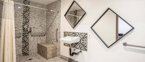 Un baño con piso de mosaico, ducha con cortina, lavamanos con espejo y barandilla.