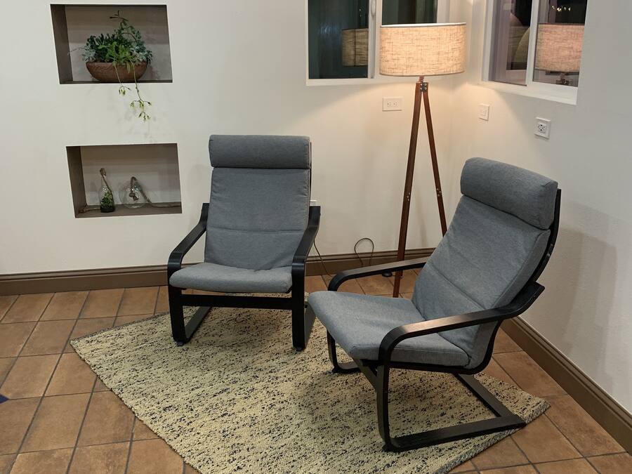 A room with two grey armchairs, a patterned rug, a floor lamp, and wall-mounted shelves with decorative items.