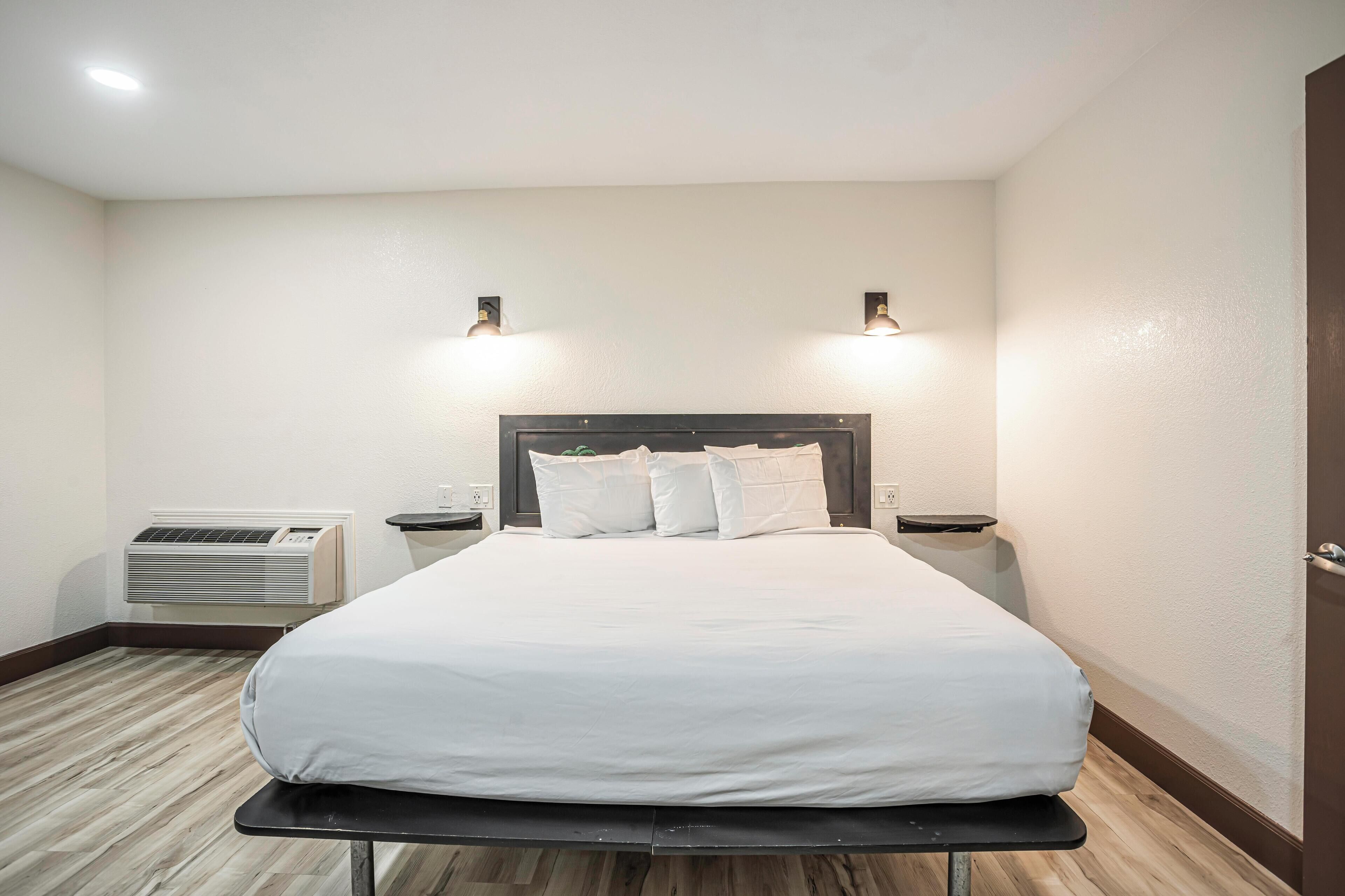 Habitación de hotel con cama, dos mesitas de noche, aire acondicionado de pared y dos luces de pared.