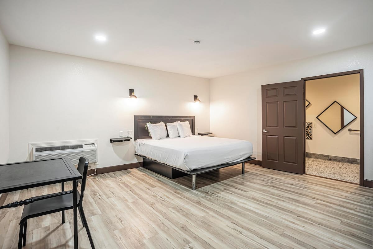 A bedroom with a bed, bedside tables, a desk, and a chair. There is a door and a wall-mounted mirror.